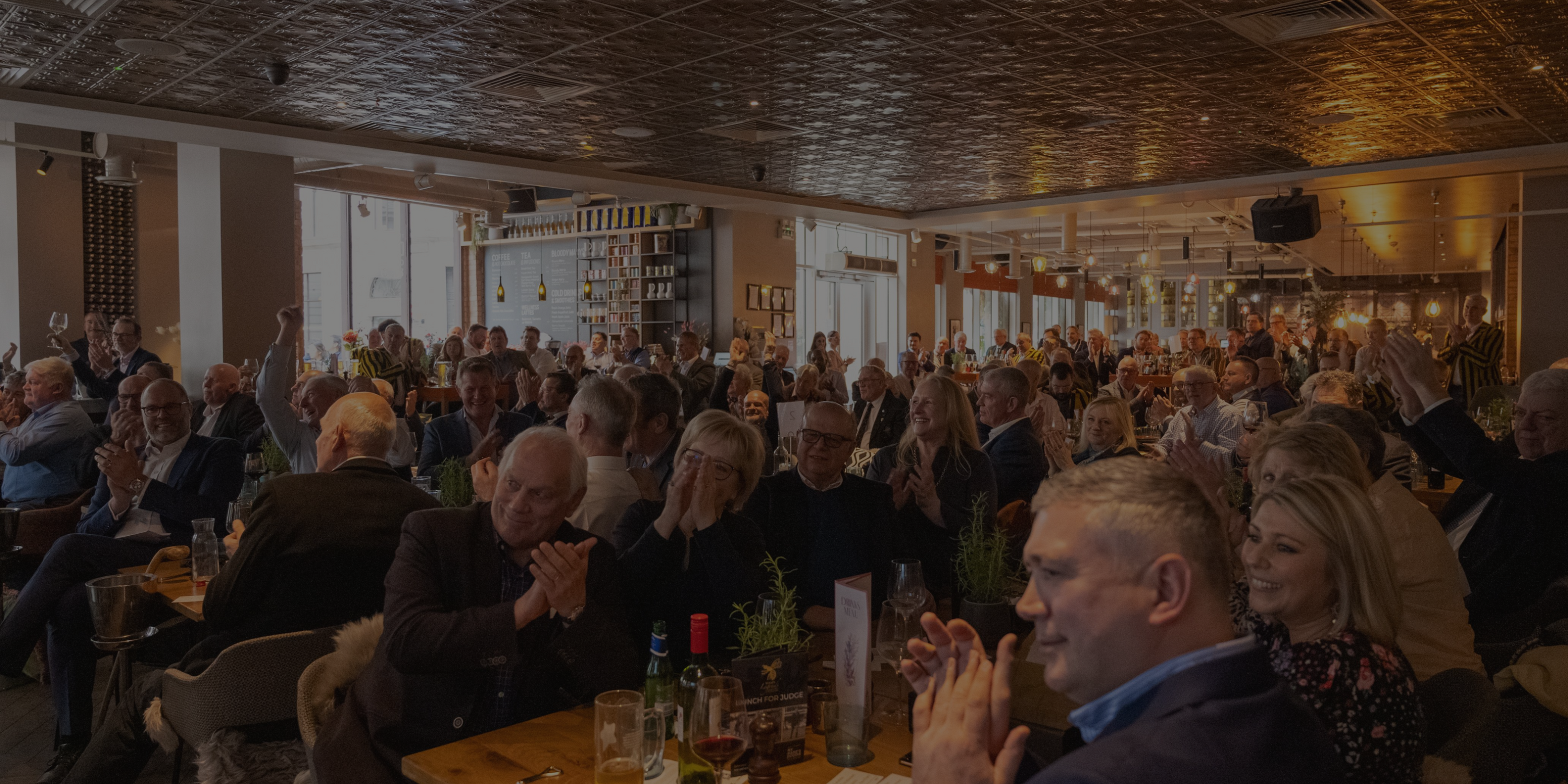 Attendees at Lunch for Judge applauding an appearance on screen from Paul Rendall at the Anthologist, London 